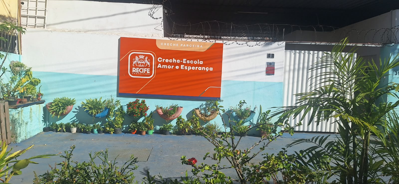 Fachada da Creche-Escola Amor e Esperança, com placa de identificação e plantas no pátio de entrada.