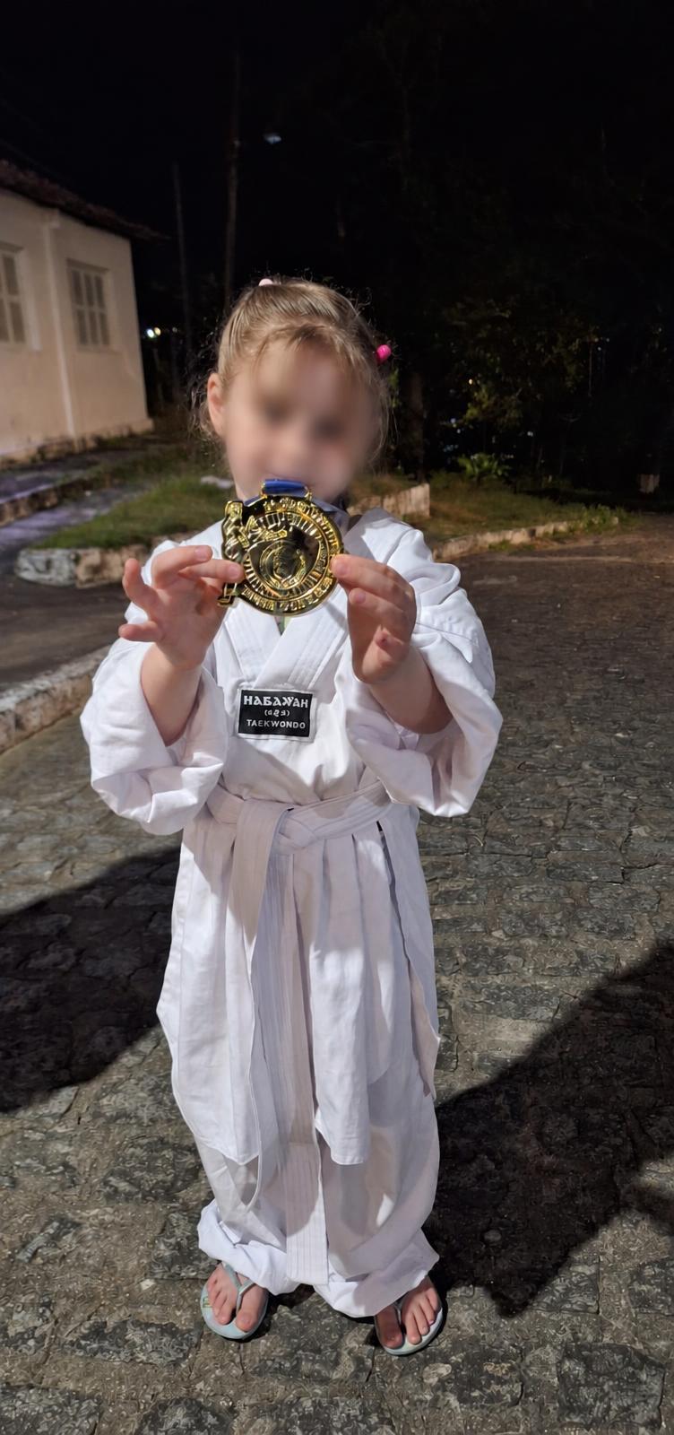 Criança de uniforme de taekwondo mostrando uma medalha.
