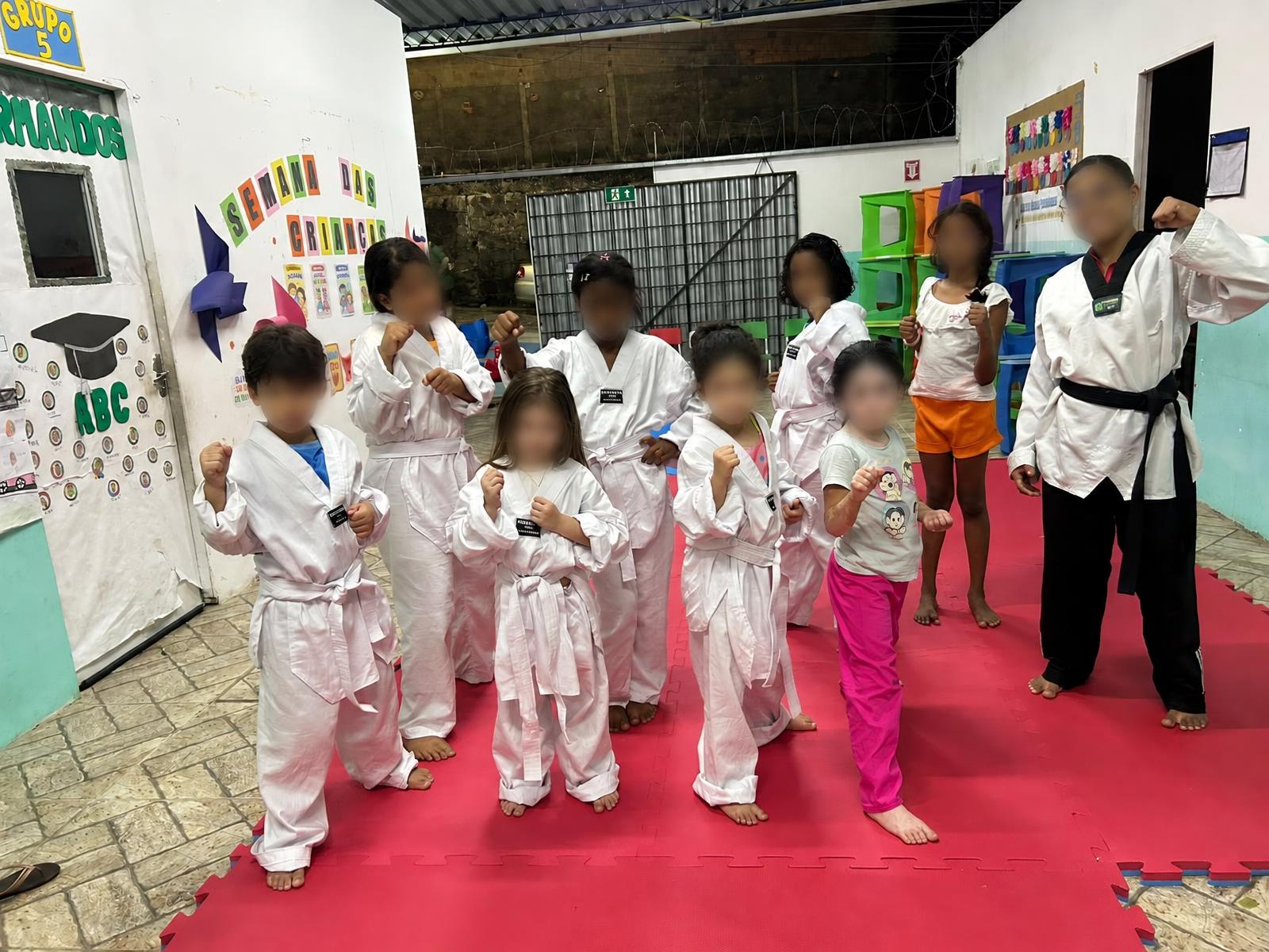 Crianças e instrutora reunidas no espaço de treino de taekwondo.
