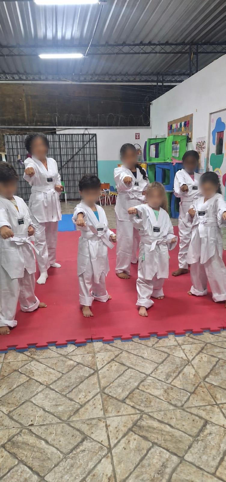 Crianças e adulta praticando posições de taekwondo no tatame.